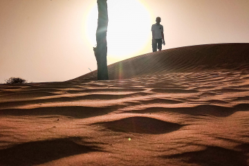 Mann auf Düne in Wüste, Sonne im Hintergrund